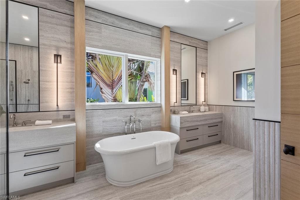 Full bath featuring vanity, healthy amount of natural light, a freestanding tub, recessed lighting, and tile walls