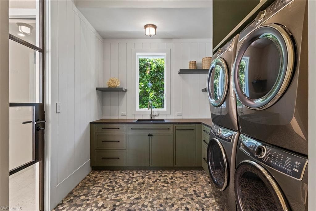 Laundry room featuring wood walls, dark flooring, cabinet space, and washer and clothes dryer