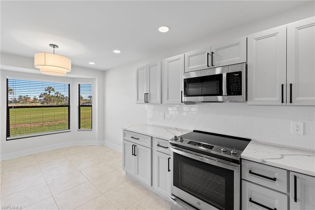 Kitchen with stainless steel appliances, pendant lighting, light stone countertops, light tile patterned floors, and backsplash