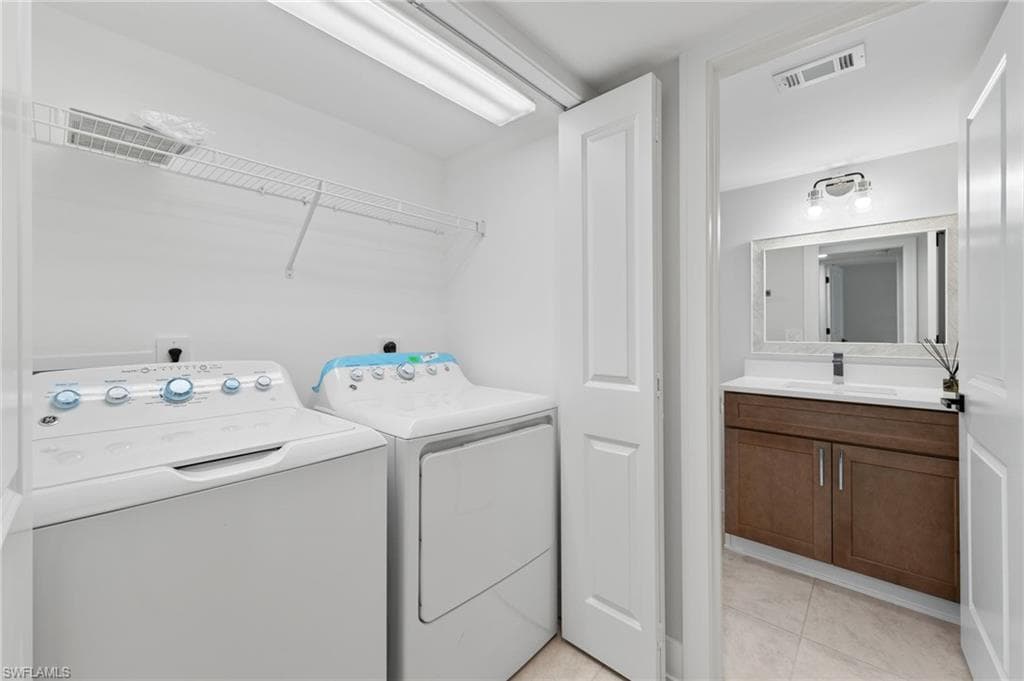 Clothes washing area featuring light tile patterned flooring, washer and clothes dryer, and sink