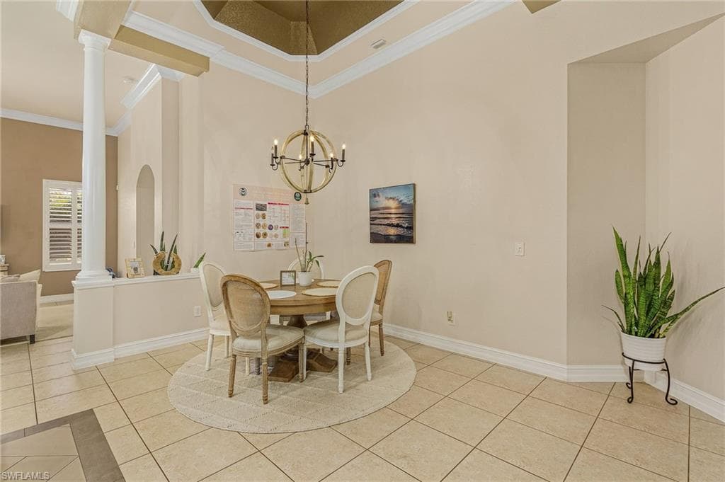 Dining area featuring crown molding, decorative columns, light tile flooring, a notable chandelier, and a high ceiling