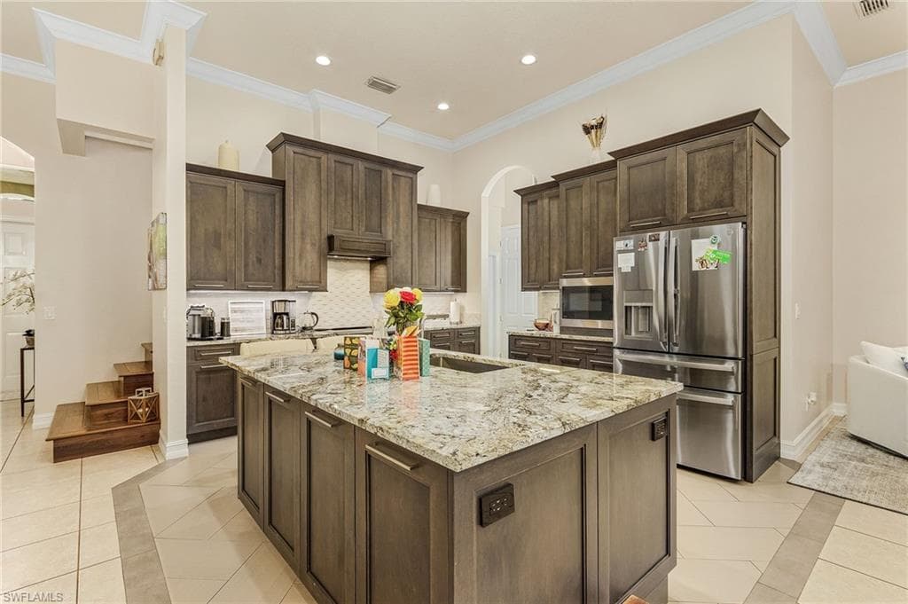 Kitchen featuring a center island with sink, crown molding, backsplash, and appliances with stainless steel finishes