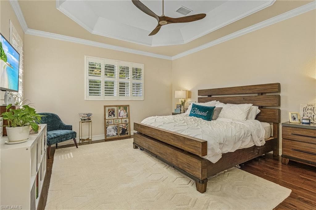 Bedroom with ornamental molding, hardwood / wood-style floors, ceiling fan, and a raised ceiling