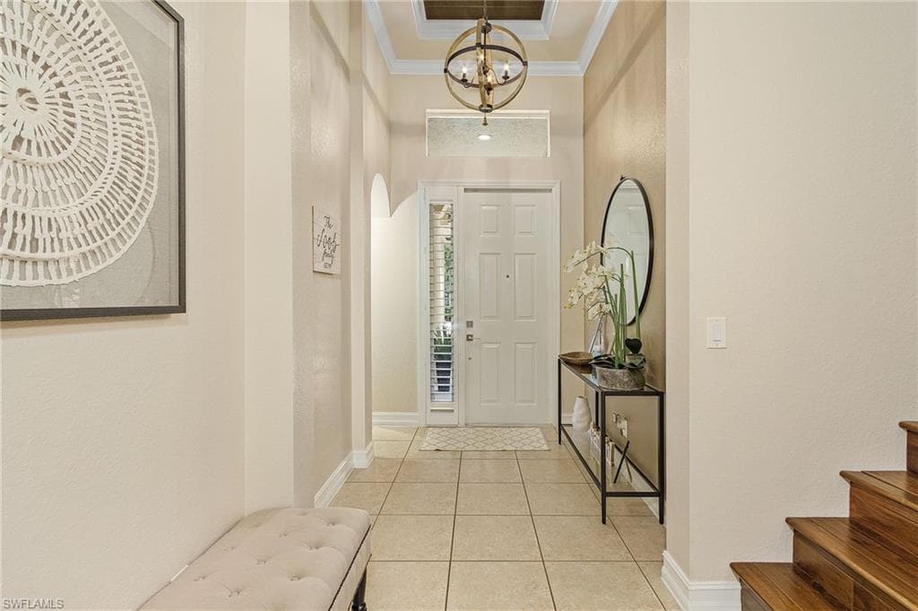 Foyer featuring an inviting chandelier, a tray ceiling, light tile floors, and crown molding