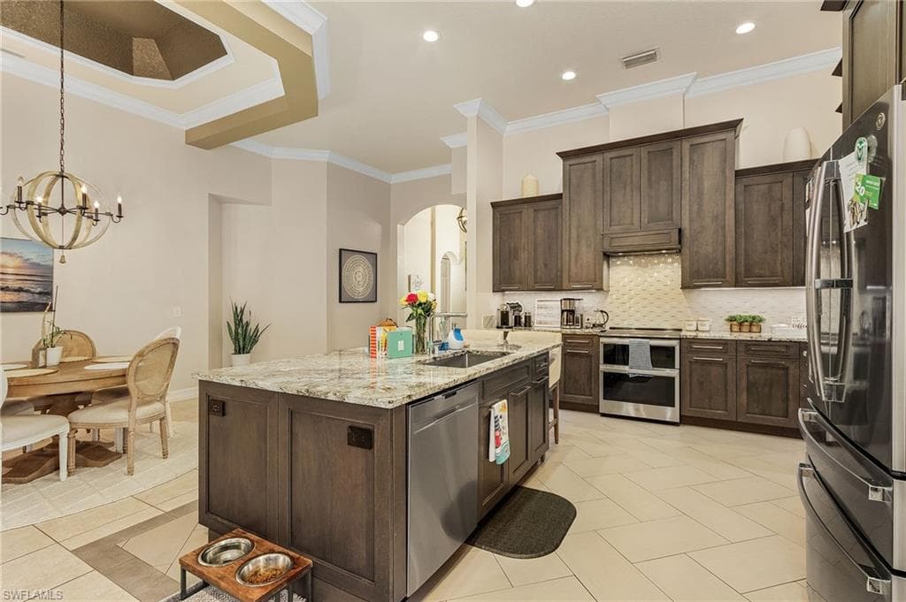 Kitchen featuring ornamental molding, stainless steel appliances, a kitchen island with sink, tasteful backsplash, and light tile floors
