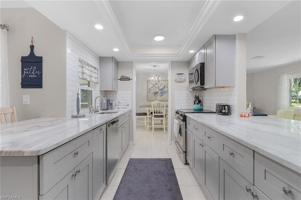 Kitchen with a tray ceiling, backsplash, light stone counters, and stainless steel appliances