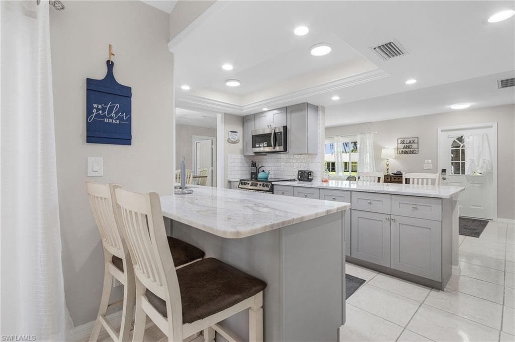 Kitchen with a center island, stainless steel appliances, gray cabinets, backsplash, and a raised ceiling