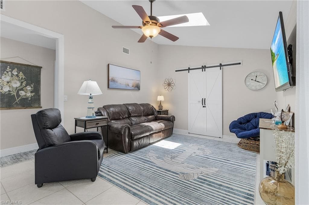 Tiled living room with a barn door, ceiling fan, a skylight, and high vaulted ceiling