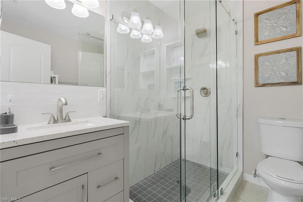 Bathroom with backsplash, vanity with extensive cabinet space, toilet, a shower with shower door, and tile flooring
