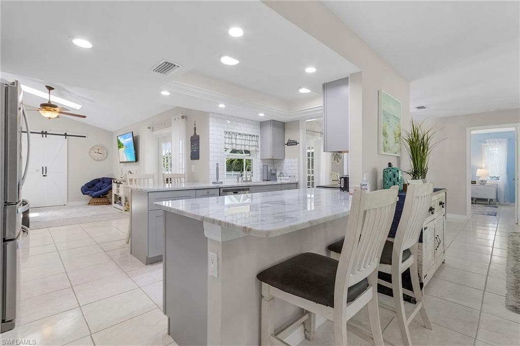 Kitchen with kitchen peninsula, light stone counters, a kitchen bar, ceiling fan, and light tile floors