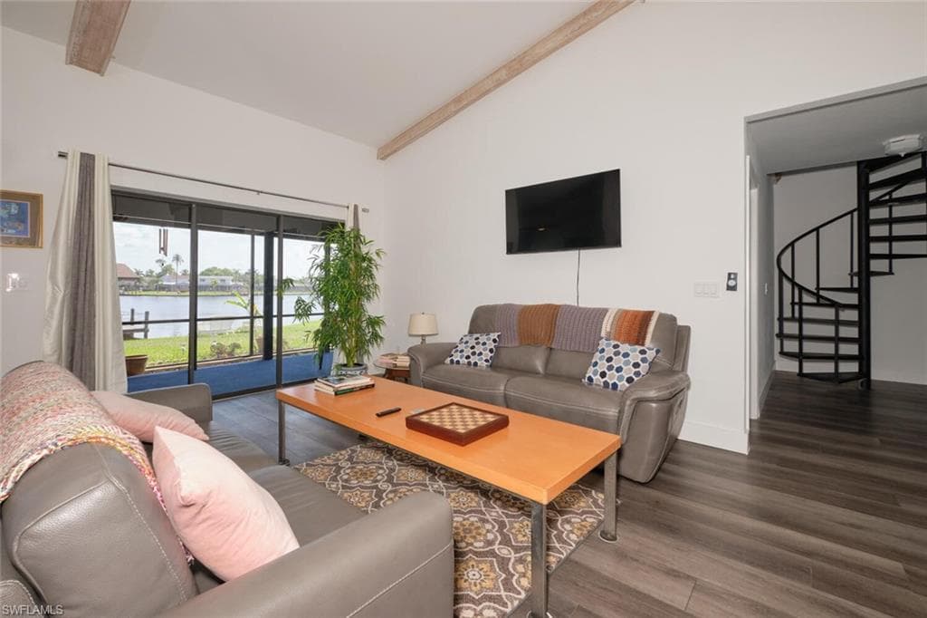 Living room featuring dark hardwood / wood-style flooring, vaulted ceiling with beams, and a water view