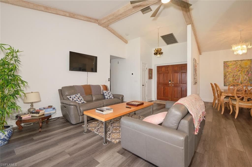 Living room featuring ceiling fan with notable chandelier, hardwood / wood-style flooring, and beam ceiling