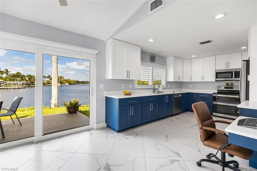Kitchen with a river view, blue cabinetry, white cabinetry, quartz counter tops, stainless steel appliances, porcelain tile floors. Built in desk on right side of photo.