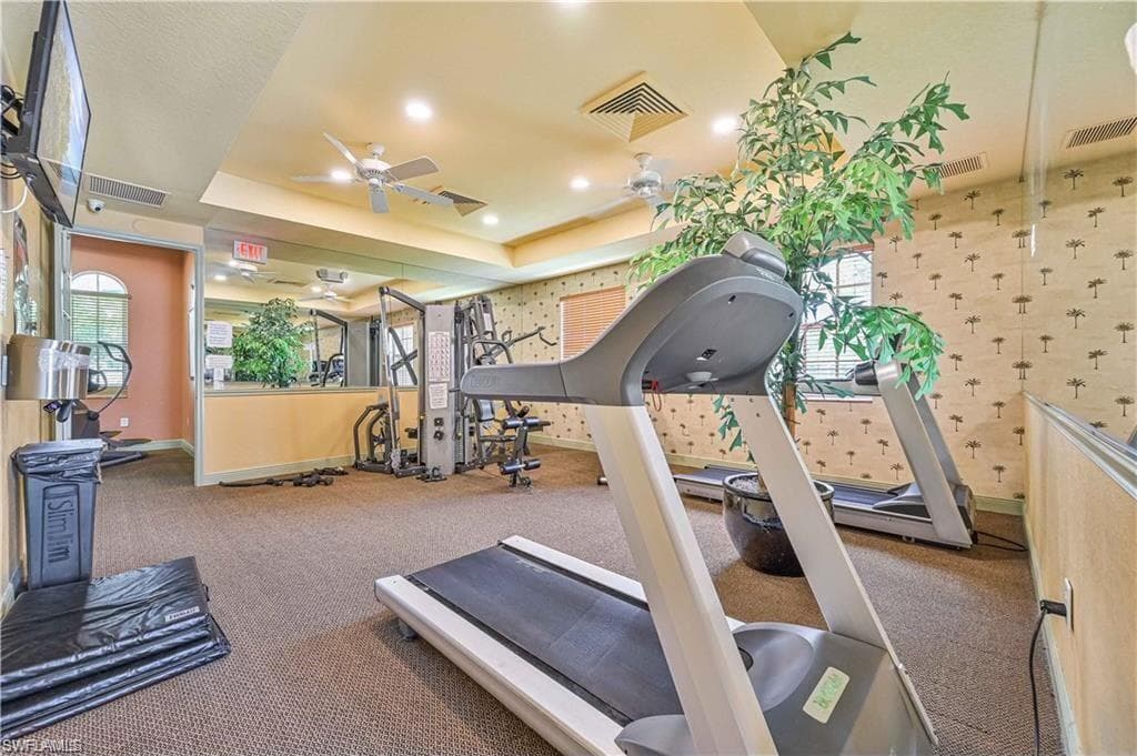 Gym with a tray ceiling, ceiling fan, and carpet floors