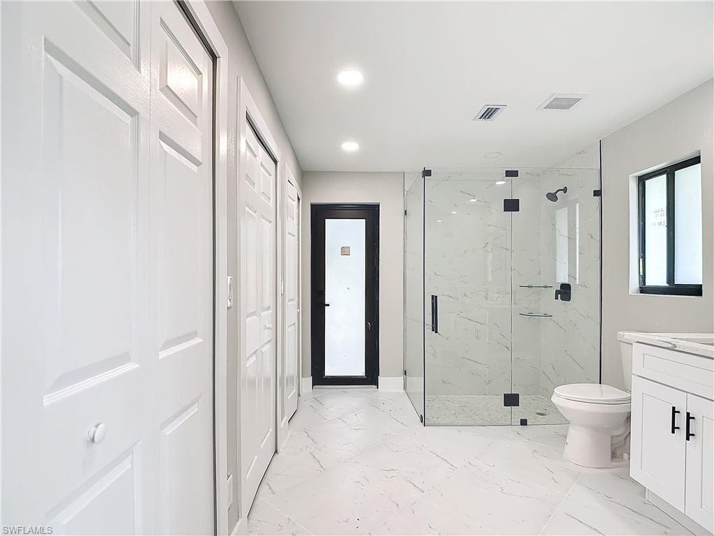 Bathroom with tile floors, a shower with shower door, vanity, and toilet