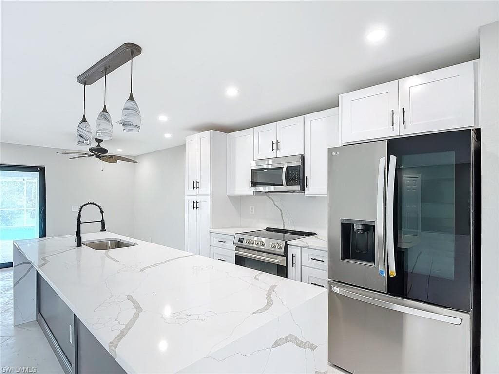 Kitchen featuring ceiling fan, stainless steel appliances, decorative light fixtures, and a kitchen island with sink
