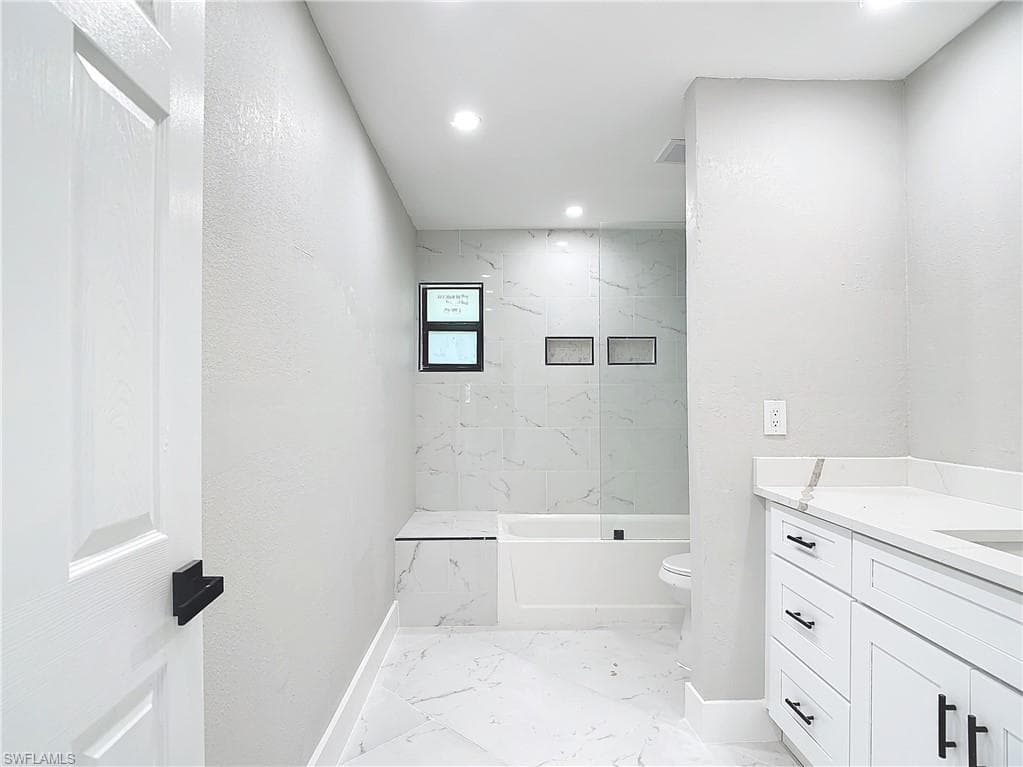 Full bathroom with tiled shower / bath, vanity, toilet, and tile floors
