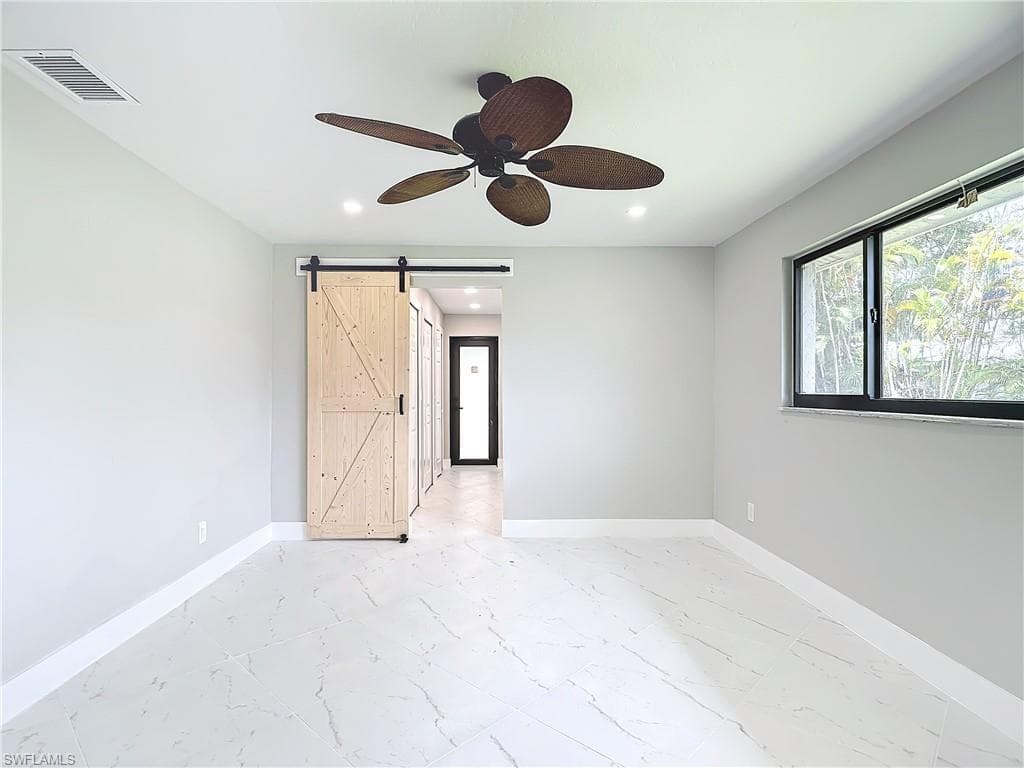 Empty room with a barn door, ceiling fan, and light tile flooring