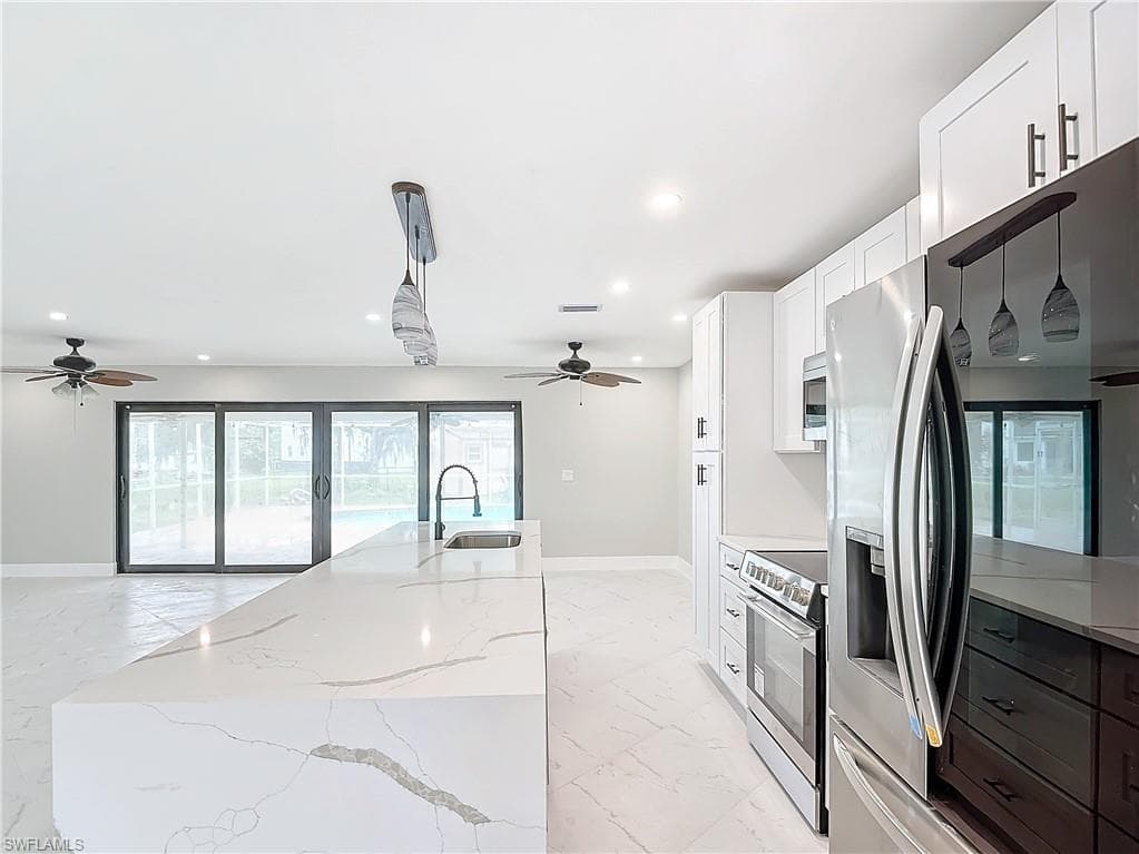 Kitchen with decorative light fixtures, stainless steel appliances, a center island, white cabinets, and light tile floors