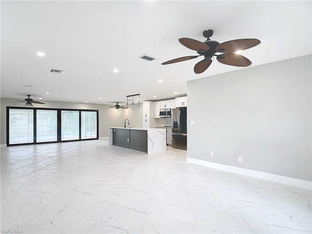 Unfurnished living room with sink, ceiling fan, and light tile floors