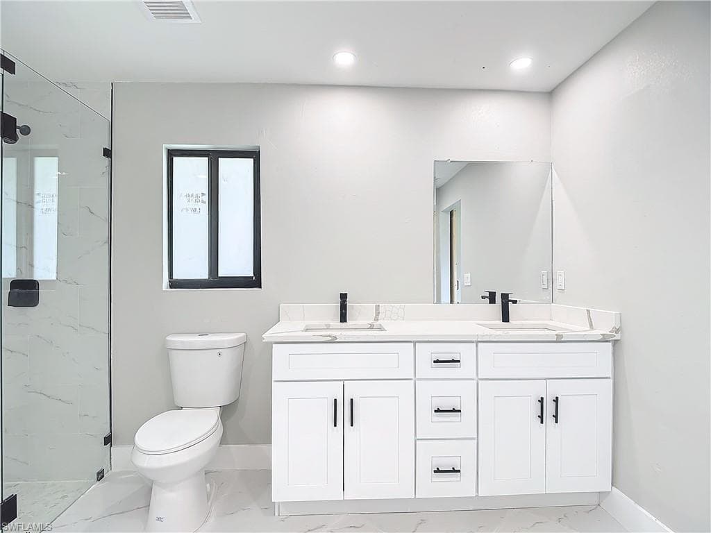 Bathroom featuring oversized vanity, dual sinks, toilet, tile flooring, and a shower with door