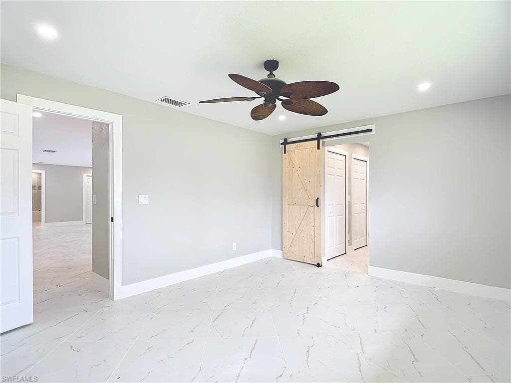 Unfurnished bedroom with a barn door, ceiling fan, and light tile flooring