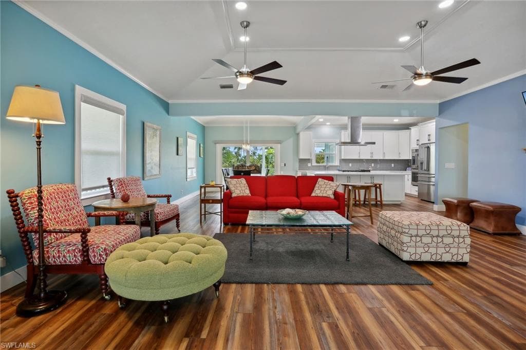 Living room featuring wood-type flooring, ceiling fan with notable chandelier, and crown molding
