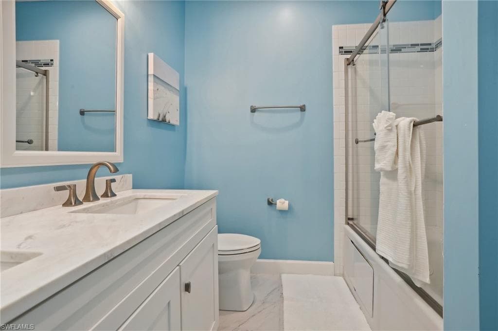 Full bathroom with bath / shower combo with glass door, vanity, tile patterned floors, and toilet
