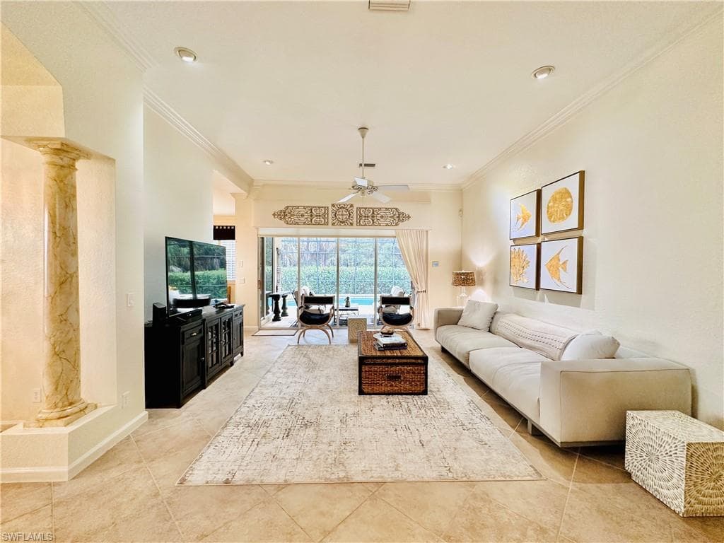 Tiled living room featuring crown molding, decorative columns, and ceiling fan
