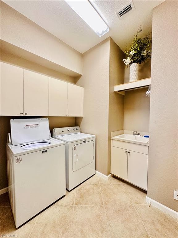 Clothes washing area featuring light tile patterned floors, a textured ceiling, washer and dryer, cabinets, and sink