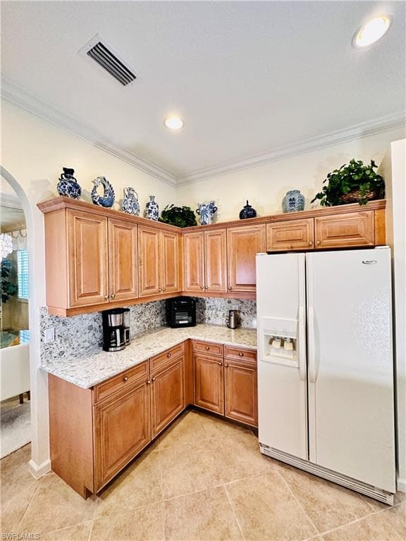 Kitchen with light tile patterned flooring, crown molding, and white fridge with ice dispenser