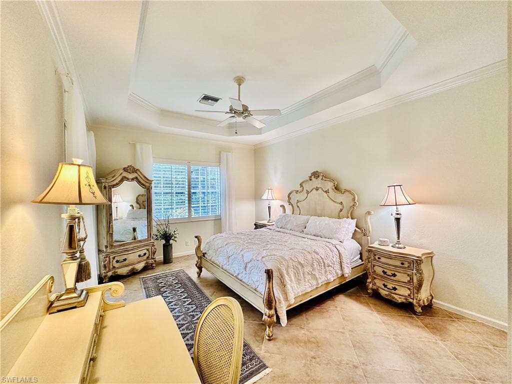 Bedroom with ornamental molding, light tile patterned flooring, ceiling fan, and a tray ceiling