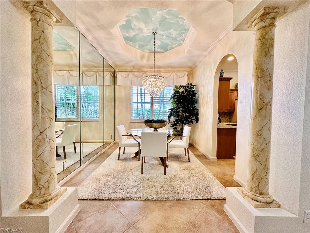 Tiled dining area with an inviting chandelier, a tray ceiling, ornate columns, and ornamental molding