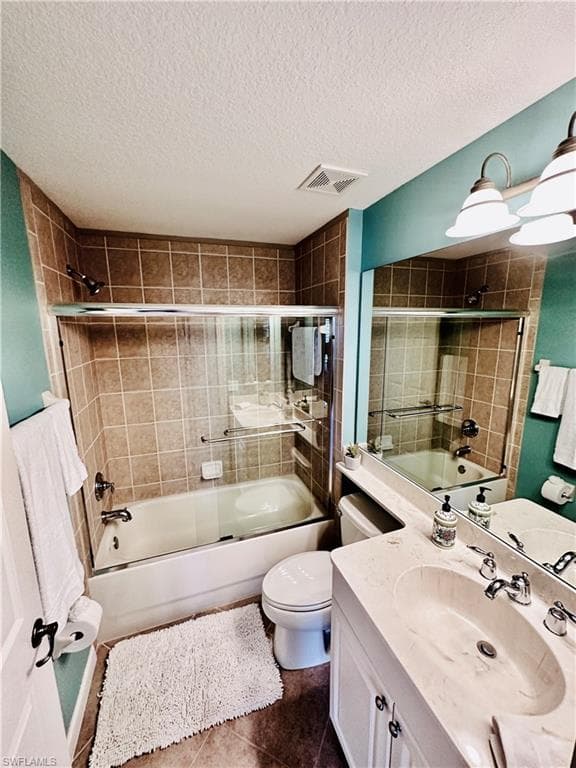 Full guest bathroom featuring vanity, tile patterned floors, combined bath / shower with glass door, toilet, and a textured ceiling