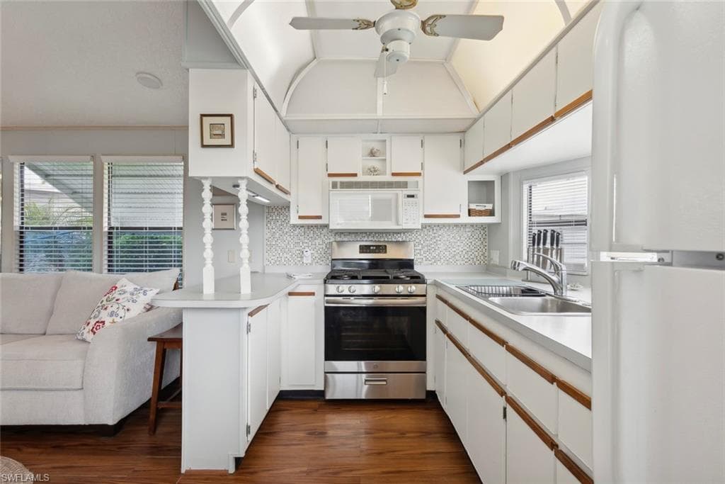 Kitchen featuring white appliances, dark hardwood / wood-style floors, decorative backsplash, sink, and white cabinetry