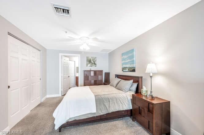 Bedroom with ceiling fan, light colored carpet, and a closet