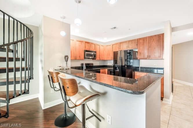 Kitchen with light wood-type flooring, a breakfast bar area, hanging light fixtures, kitchen peninsula, and stainless steel appliances