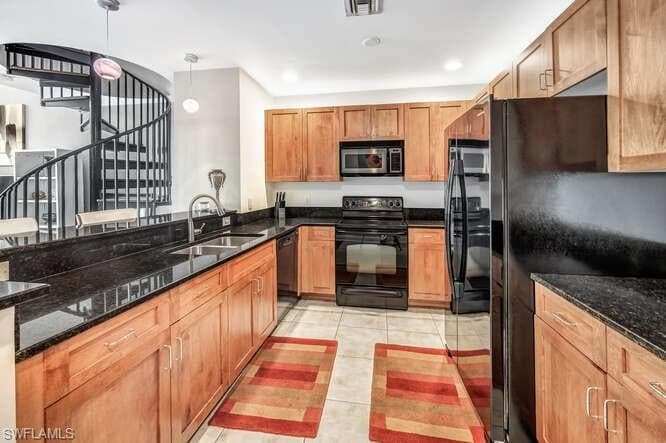 Kitchen with dark stone counters, black appliances, pendant lighting, and light tile patterned floors