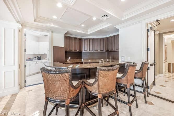 Kitchen featuring a kitchen breakfast bar, light tile patterned flooring, dark stone counters, and dark brown cabinetry