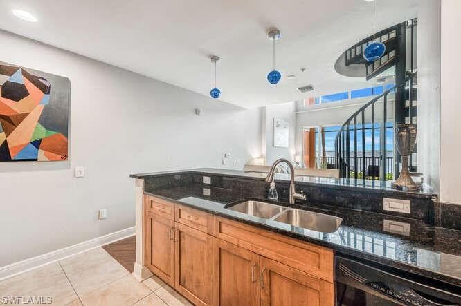 Kitchen featuring dishwasher, sink, dark stone counters, light tile patterned flooring, and hanging light fixtures