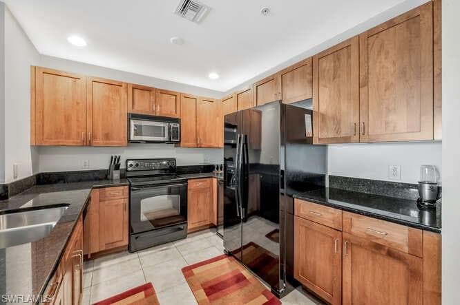 Kitchen featuring light tile patterned flooring, dark stone counters, and black appliances
