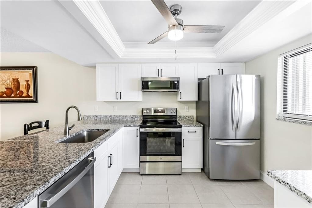 Kitchen with stainless steel appliances, sink, white cabinets, a tray ceiling, and ceiling fan