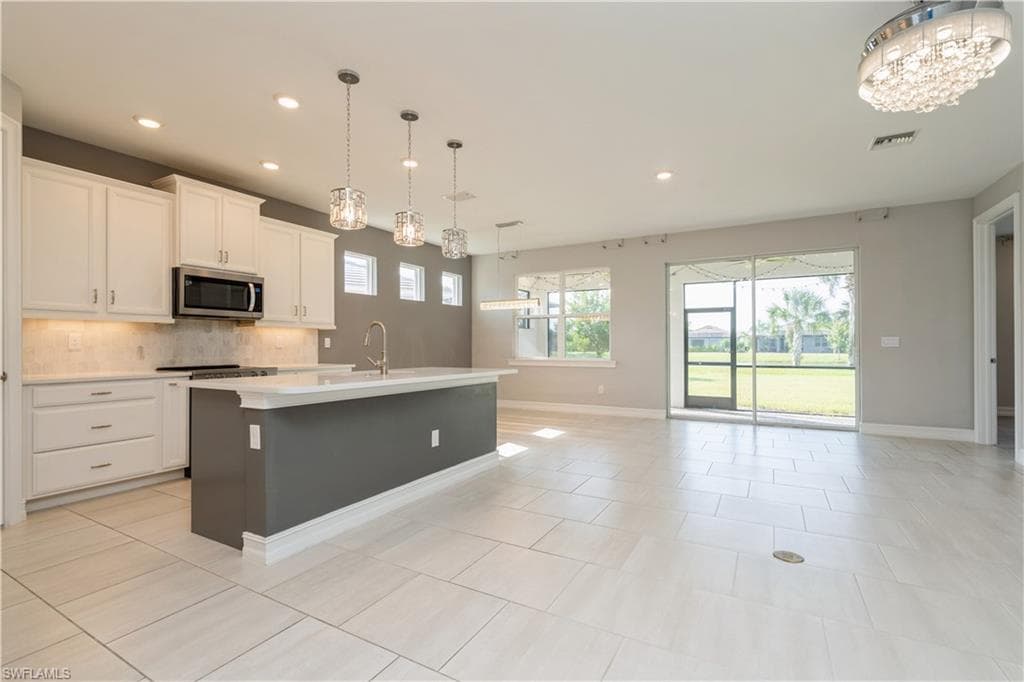 Kitchen featuring light tile patterned flooring, white cabinetry, backsplash, and an island with sink