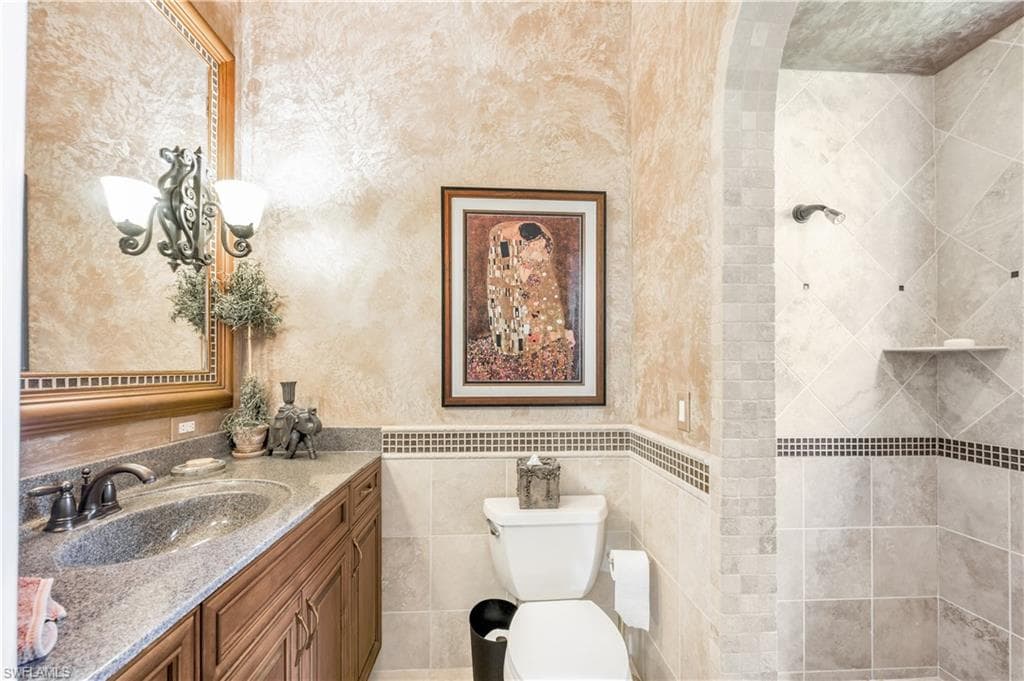 Bathroom featuring vanity, toilet, tile walls, and a tile shower