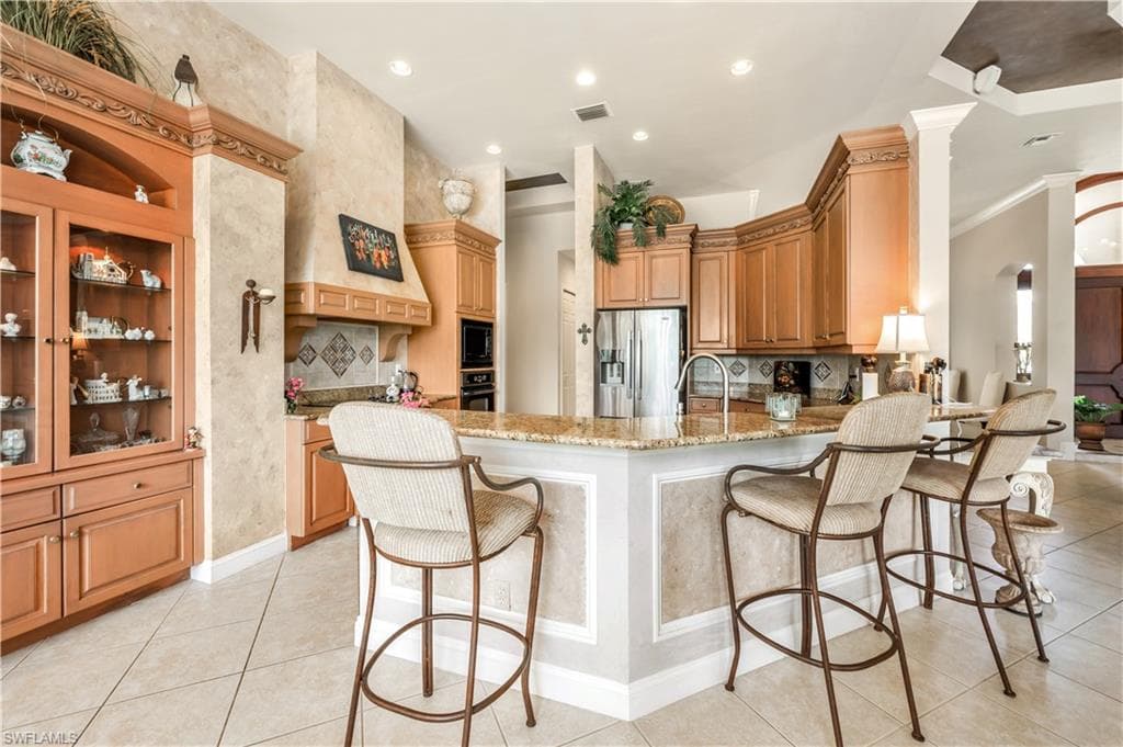 Kitchen with light stone countertops, black appliances, kitchen peninsula, light tile patterned flooring, and a kitchen breakfast bar