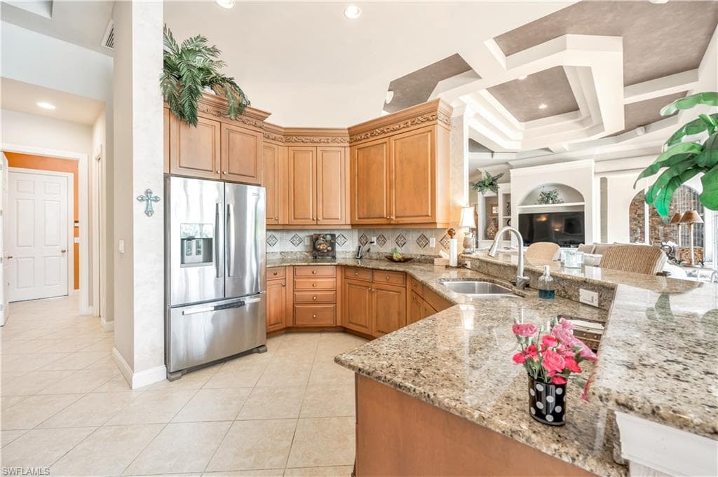 Kitchen featuring light stone countertops, sink, coffered ceiling, light tile patterned flooring, and stainless steel refrigerator with ice dispenser