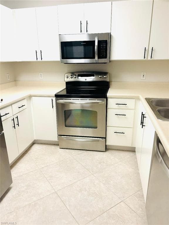 Kitchen featuring light tile patterned floors, white cabinets, appliances with stainless steel finishes, and sink