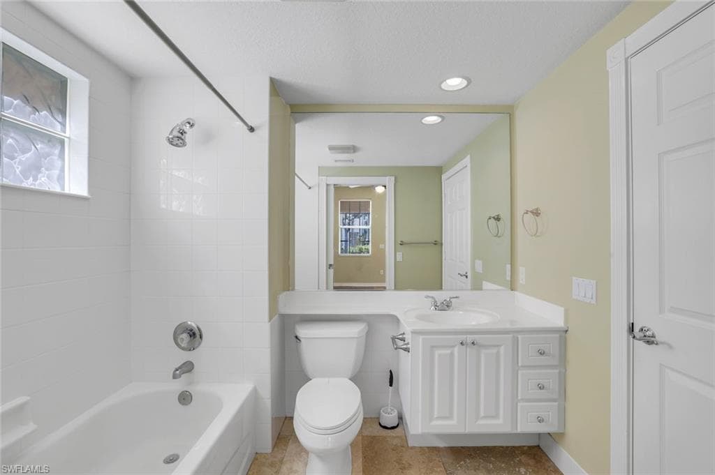 Full bathroom featuring a wealth of natural light, toilet, tiled shower / bath, and vanity