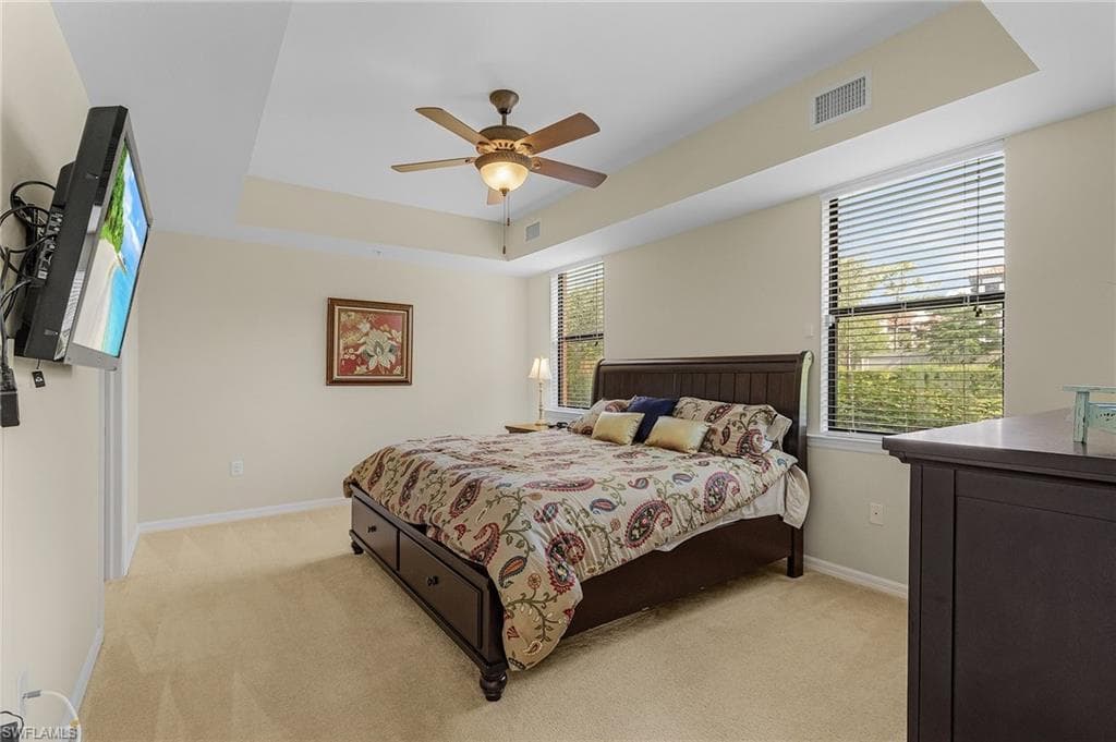Bedroom with a raised ceiling, ceiling fan, and light carpet
