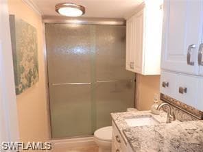 Bathroom with ornamental molding, vanity, toilet, and a shower with door